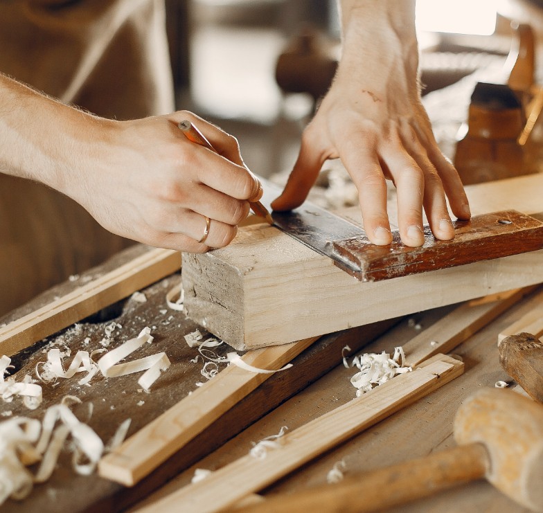 Experienced carpenter smoothing wood with hand plane on workbench.